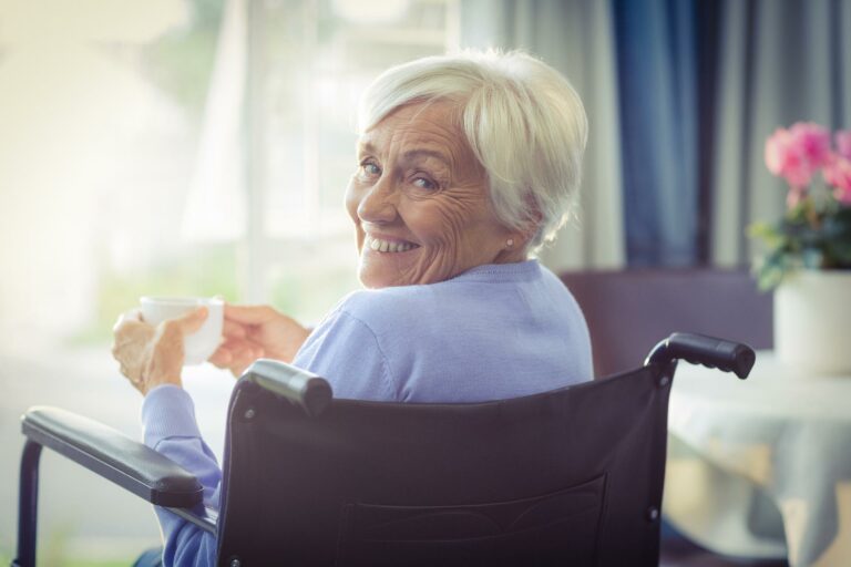 happy senior woman on wheelchair holding a cup of tea at home